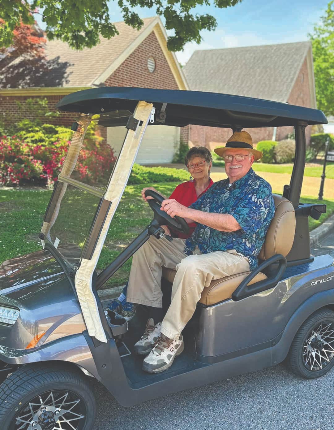 Man and woman sitting in golf cart in front of a Garden Home