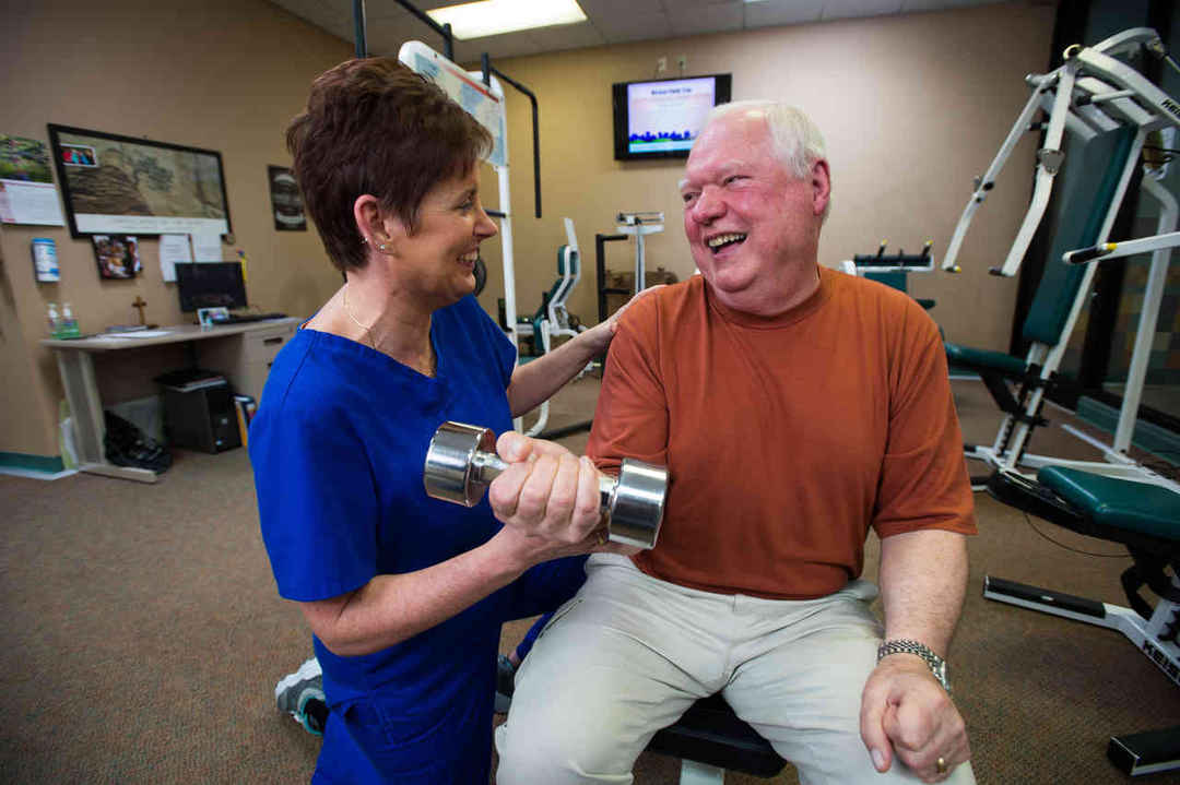 Care taker helping man train in the gym with a dumbbell