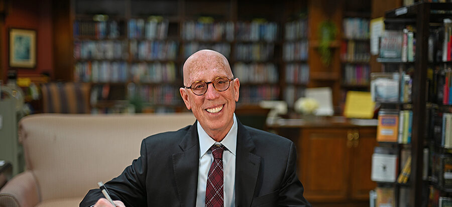 bald senior man in suit and glasses at desk with papers