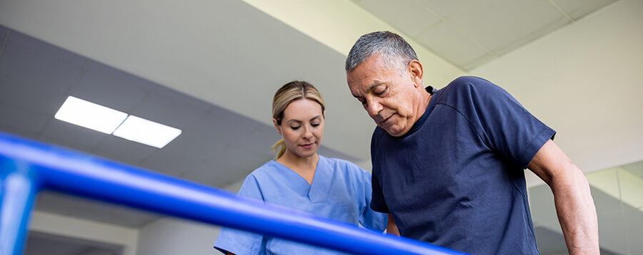 Latin American man doing physical therapy and walking on bars with the assistance of his physical therapist